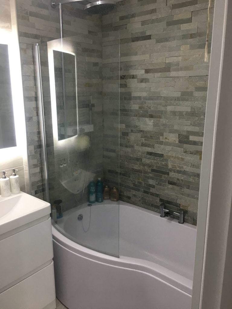 Backlit mirror next to a power shower surrounded by grey slate wall tiles