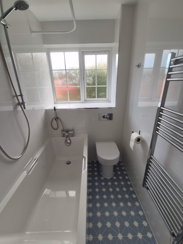 Modern bathroom renovation with patterned vinyl flooring, wall panels, vanity unit, and bath installed by DSB Bathrooms in Devon.