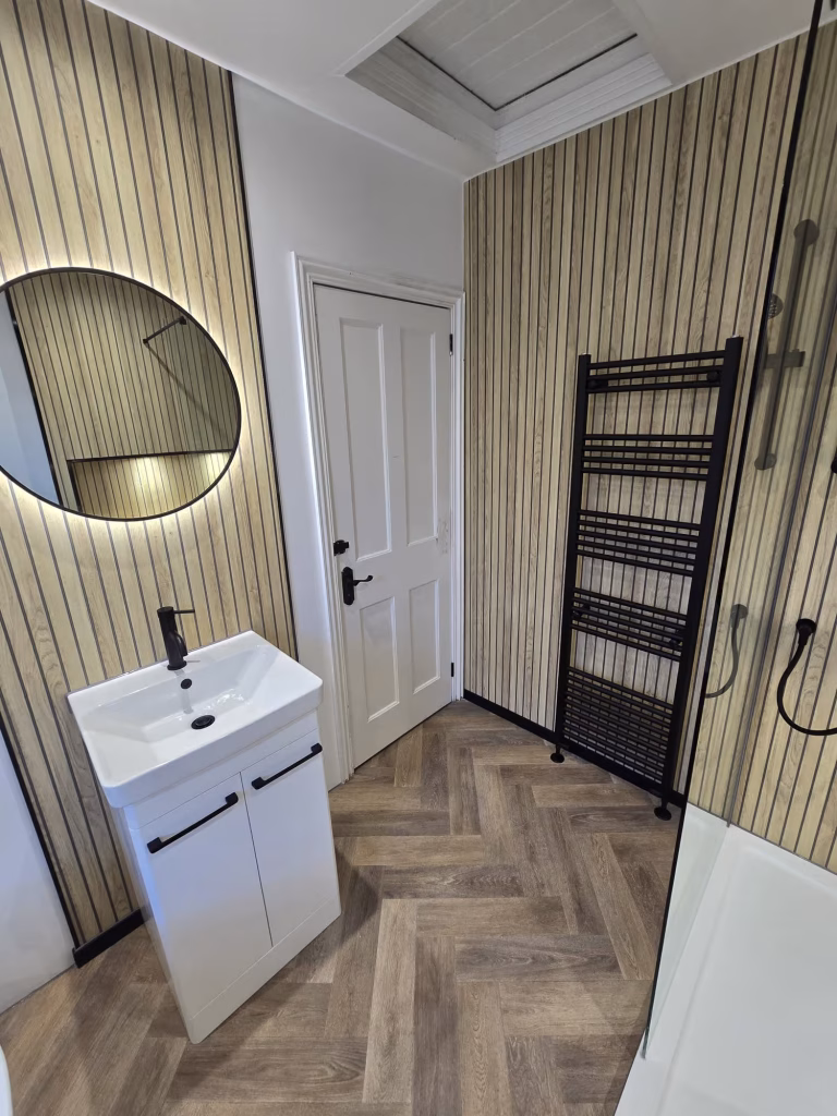 Luxury bathroom renovation featuring a freestanding bath, walk-in shower, oak slatted wall panels, black fittings, and LED mirror installed by DSB Bathrooms in Devon.